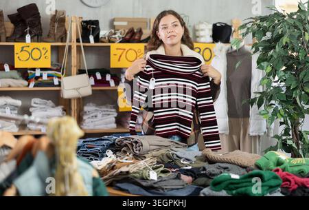 Una giovane donna sceglie un maglione nel negozio di abbigliamento Foto Stock