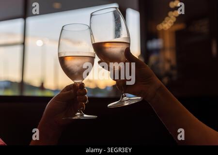 Due persone che brindono un bicchiere di vino rosato ghiacciato al tramonto durante una cerimonia aziendale serale a Brisbane. Foto Stock