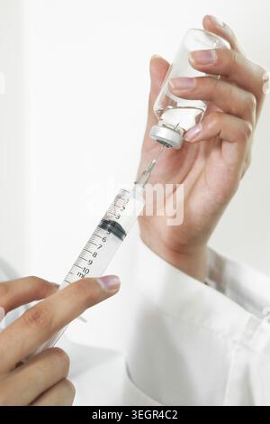 Un medico sta preparando attentamente una siringa con un farmaco da un flaconcino di vetro in un ambiente sterile di laboratorio. Foto Stock