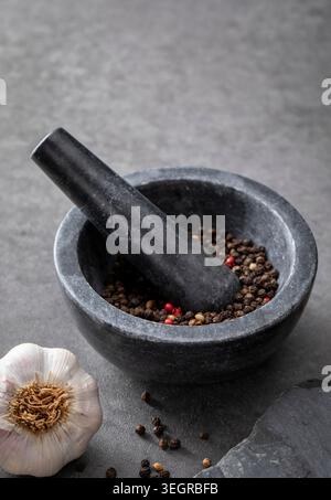 Un mortaio e un pestello pieni di grani di pepe siedono su un banco di pietra. Foto Stock