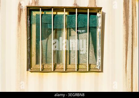 Finestra barrata su una parete intemprata con tenda blu Foto Stock