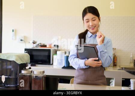 Giovane donna asiatica proprietaria di caffè, imprenditrice che utilizza un tablet digitale per gestire le attività aziendali nella cucina del bar Foto Stock