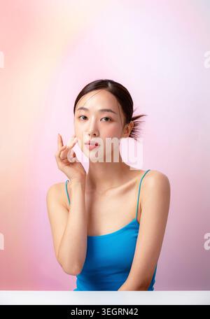 Una giovane donna con una canotta blu tocca la guancia con la mano sinistra. Foto Stock