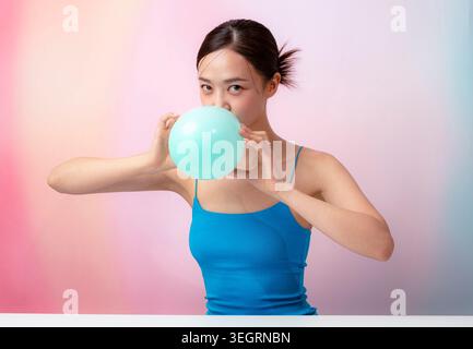 Una giovane donna si siede a una scrivania, soffiando una grande bolla con la sua gomma blu. Foto Stock