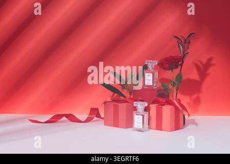 Una selezione di profumi e rose è presentata su una superficie bianca, circondata da scatole regalo rosse e un nastro rosso. Foto Stock