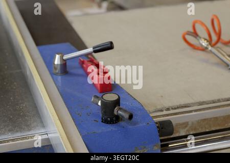 Primo piano di una macchina per la lavorazione del legno industriale con pannello di controllo blu, fermi metallici, guida di sicurezza rossa e manopole di regolazione, che enfatizzano la precisione, il calibro Foto Stock
