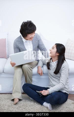 Madre sorridente e figlia studentessa delle scuole medie con un notebook Foto Stock