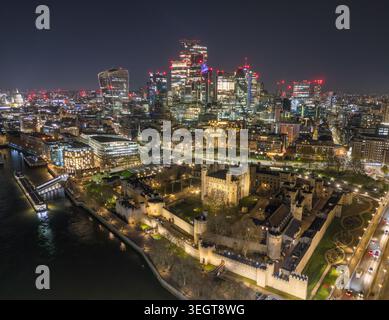 Torre di Londra di notte, illuminata accanto al Tamigi con mura storiche, torri e luci della città. Foto Stock