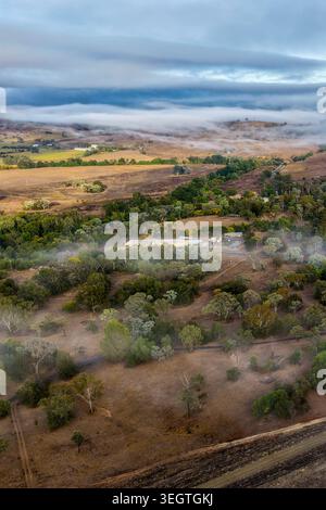 Vista verticale aerea di un paesaggio nebbioso lungo la parete della diga di Glenbawn nel nuovo Galles del Sud Australia. La fotografia del drone cattura le nuvole basse che si spostano attraverso. Foto Stock