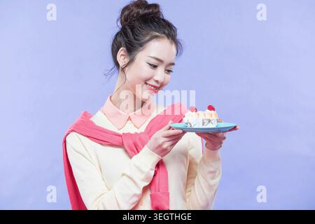 Una giovane donna tiene una fetta di torta davanti a uno sfondo azzurro. Foto Stock