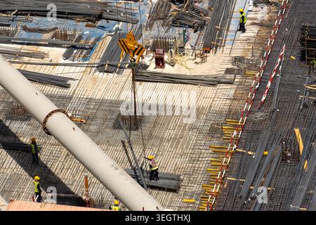 Vista aerea di un cantiere affollato con lavoratori in attrezzature di sicurezza che posano tondini in acciaio vicino a un grande gancio per gru e tubazioni industriali a Dubai, Dubai, Foto Stock