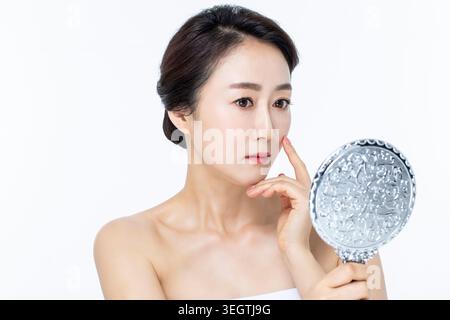 Una donna dei primi anni '30, con i capelli scuri, applica il trucco davanti a uno specchio. Foto Stock