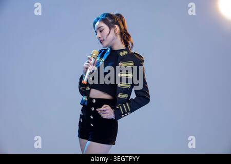 Una giovane donna con un vestito da palcoscenico tiene un microfono e sorride al pubblico. Foto Stock