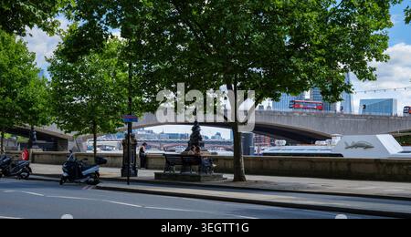 Londra - 07 09 2022: Persone sedute sul Victoria Embankment con Waterloo Bridge sullo sfondo Foto Stock