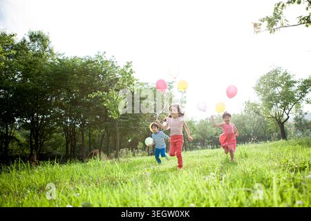Bambini sorridenti con palloncini che corrono sulla prateria Foto Stock