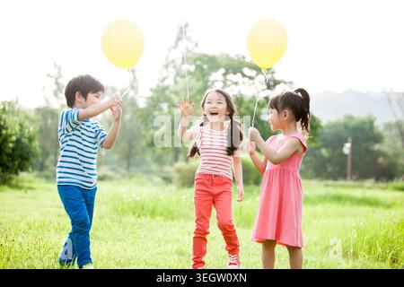 Bambini sorridenti con palloncini in piedi sulla prateria Foto Stock