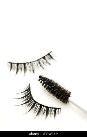 Un paio di ciglia false e una spazzola mascara sono disposte su una superficie bianca. Foto Stock