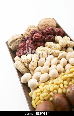 Un vassoio di legno è riempito con un assortimento di frutta a guscio e frutta secca, tra cui arachidi, mandorle, noci e datteri, allestito in un'esposizione colorata e invitante. Foto Stock