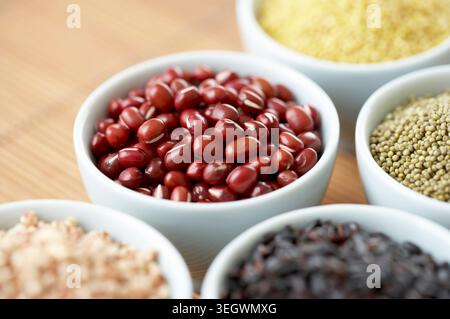 Primo piano di vari tipi di chicchi e fagioli in piccole ciotole bianche su un tavolo di legno. Foto Stock