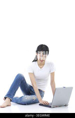 Una giovane donna seduta sul pavimento con un notebook, sorridente mentre digita la tastiera. Foto Stock