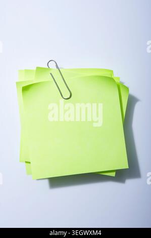 Una graffetta di colore giallo brillante contiene una pila di note adesive di colore giallo brillante su sfondo bianco. Foto Stock