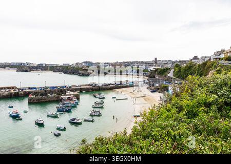 Una tranquilla vista del porto di Newquay in Cornovaglia, che mostra piccole barche che riposano in acque poco profonde accanto alla spiaggia sabbiosa. I muri di pietra del porto incorniciano la scena, Foto Stock
