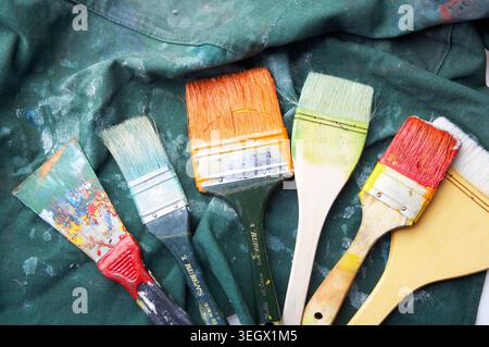 I pennelli dipinti si trovano su una tela verde, sparsi di colori vivaci. Foto Stock