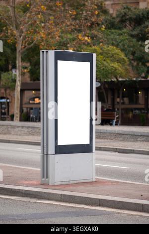 Ampio cartellone verticale con schermo digitale in piedi su un marciapiede vicino a una strada Foto Stock