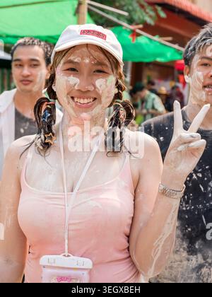 Una giovane donna sorridente coperta di polvere bianca celebra il festival di Songkran a Lampang, in Thailandia, con gli amici. Foto Stock
