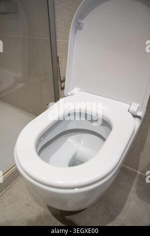 WC in ceramica bianca con coperchio aperto in un bagno moderno piastrellato, che mostra un interno pulito, igienico e ben mantenuto per l'uso quotidiano e. Foto Stock