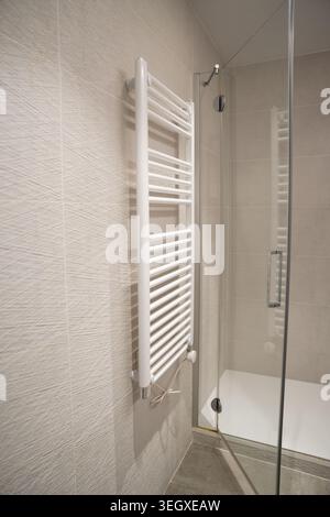 Bagno moderno con portasciugamani riscaldato bianco montato su piastrelle in ceramica testurizzata, per offrire comfort e design contemporaneo Foto Stock