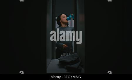 Young Athletic Woman apre l'armadietto della palestra dall'interno, cambia in abbigliamento sportivo, beve acqua e chiude la porta. Routine fitness cinematografica. Concetto di preparazione, concentrazione, privacy e stile di vita attivo. Foto Stock