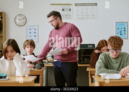Uomo di mezza età insegnante che distribuisce i test agli adolescenti in aula Foto Stock