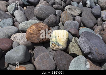 Consistenza naturale di pietre vulcaniche lisce e colorate sulla spiaggia remota di Gran Canaria, Isole Canarie, Spagna. Foto Stock