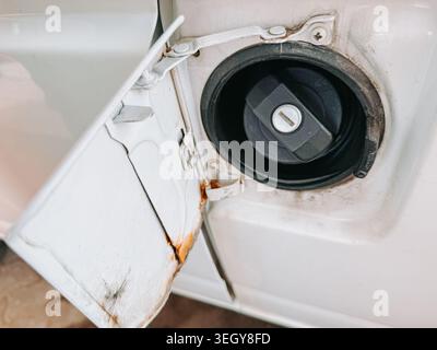 Primo piano dettagliato di un tappo del bocchettone di rifornimento del carburante aperto del veicolo con ruggine e usura visibili. Ideale per manutenzione, riparazione, impianto di alimentazione, corrosione, tra Foto Stock