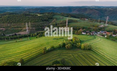 Vista aerea dei verdi campi di campagna con linee elettriche e colline forestali al tramonto nella Germania rurale Foto Stock