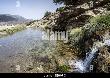 Vista di un limpido torrente di montagna e di una piccola cascata che scorre attraverso terreni rocciosi con vegetazione verde sparsa nelle montagne dell'alto Atlante tizi Oussem Foto Stock