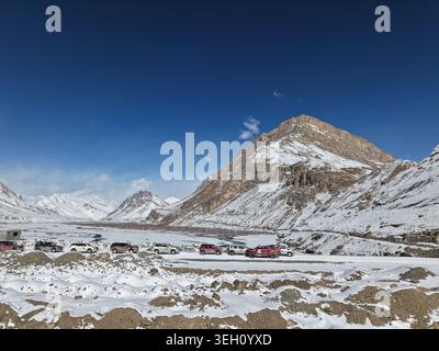 Kaza, India - 28 gennaio 2026: Vista di un convoglio di veicoli fuoristrada parcheggiati su una strada innevata nella valle di Spiti, circondato da aspre mou innevate Foto Stock