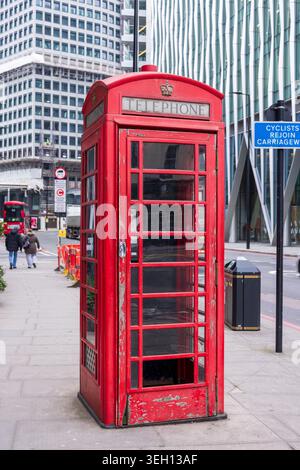 Londra, Regno Unito - 12 maggio 2025: Vista di una classica cabina telefonica rossa su un marciapiede della città con architettura moderna e pedoni nel backgroun Foto Stock