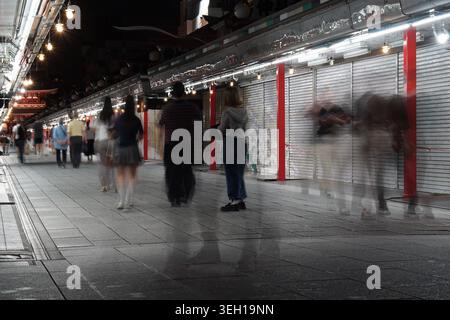 Vista notturna della via dello shopping Nakamise-dori ad Asakusa, Tokyo, con pedoni sfocati che conducono verso il Tempio senso-ji e la porta di Kaminarimon. Foto Stock
