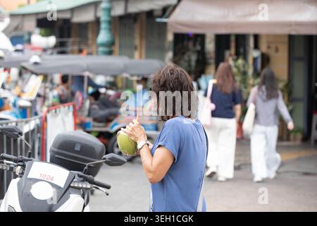 Turista che beve acqua fresca di cocco, viaggiatrice che esplora il mercato all'aperto, profilo laterale Foto Stock
