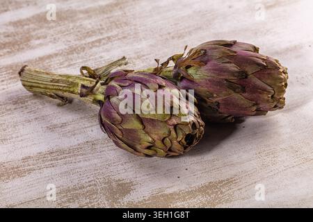 Due carciofi a globo freschi visualizzati su sfondo in legno bianco chiaro testurizzato. Sano biologico vegetale, natura morta cibo fotografia. Li naturali Foto Stock