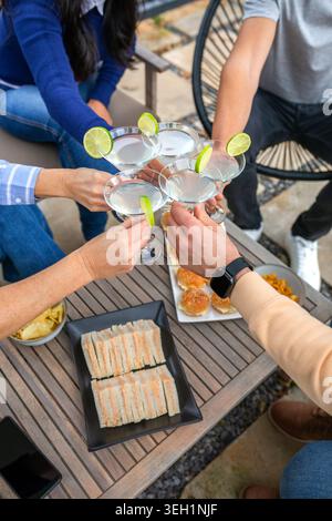 Amici felici e irriconoscibili che brindano con bevande festeggiando insieme e gustando spuntini all'aperto Foto Stock