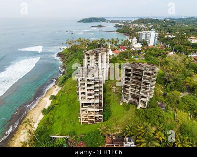 Vista aerea di edifici abbandonati in cemento su una lussureggiante scogliera verde che si affaccia sull'oceano turchese e sulla costa di Mirissa, nella provincia meridionale, Sri LAN Foto Stock