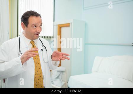 Maschio medico gesting e spiegazione nella stanza d'ospedale indossando camice da laboratorio e stetoscopio, copia spazio Foto Stock