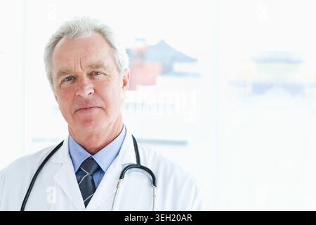 Medico di sesso maschile anziano in clinica con camice da laboratorio bianco e stetoscopio Foto Stock