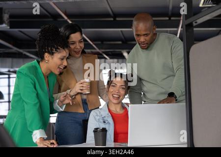 Diversi colleghi che collaborano alla scrivania in un ufficio open space, visualizzano laptop e indossano abiti da lavoro. Lavoro di squadra, colleghi, spazio di lavoro, luce del giorno, moderno, industriali, divisori Foto Stock