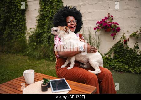 Donna nera felice che abbraccia il cane da compagnia nel cortile Foto Stock