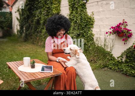 Giovane donna seduta nel cortile, che accarezza il cane felice Foto Stock