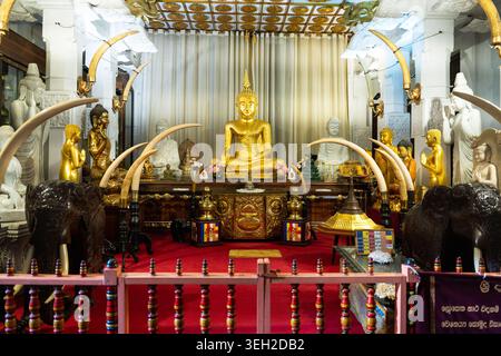 Vista dell'interno ornato del Tempio della reliquia del Sacro dente con una statua di Buddha dorata circondata da zanne d'avorio e sculture bianche Ka Foto Stock
